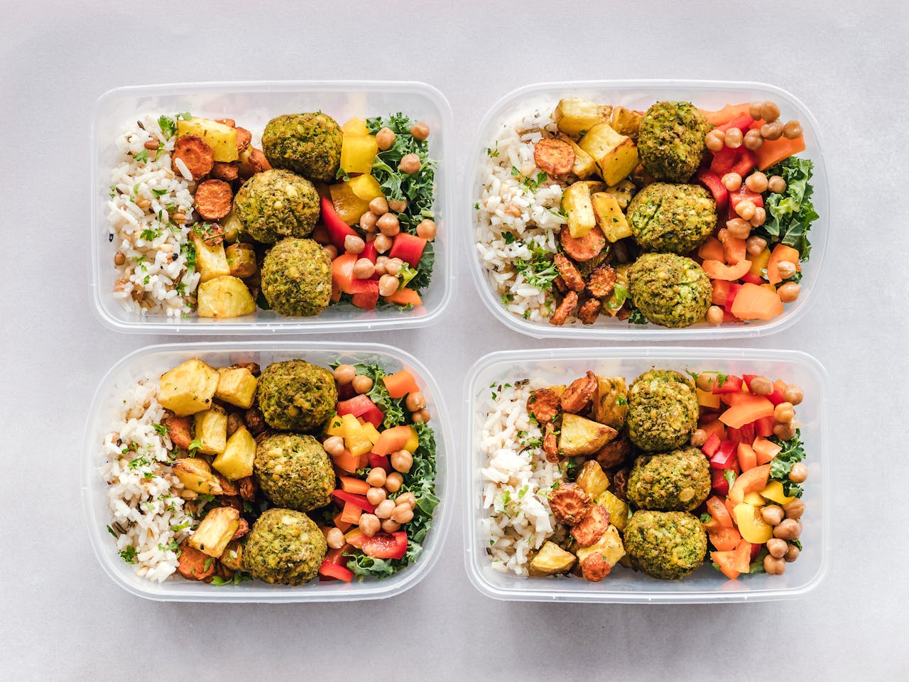 Colorful meal prep containers with falafel, chickpeas, rice, and vegetables for a healthy lifestyle.